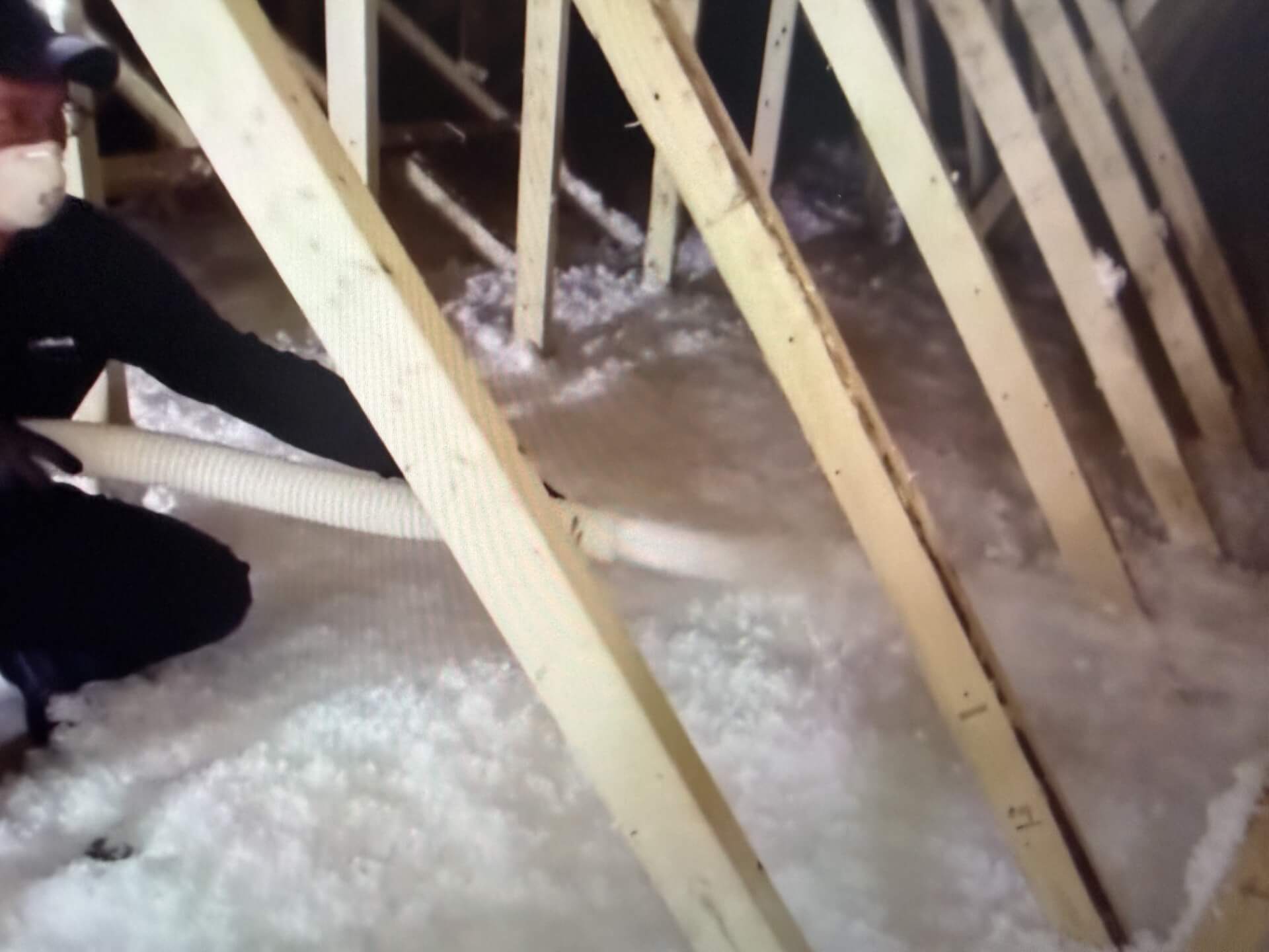 blown in fiberglass being sprayed by a man in an attic with wooden structural construction